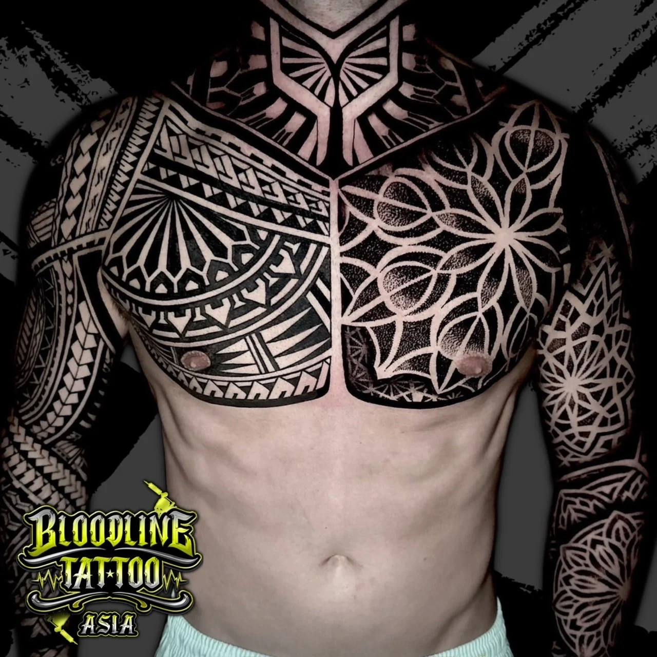 Torso tattoo mixing chest mandala dotwork, geometric neck bands, and bold blackwork tribal patterns across both arms, at Bloodline Tattoo Bangkok.