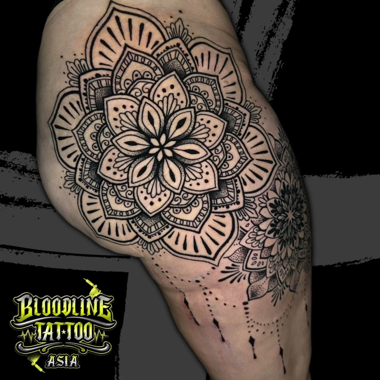 Upper-leg mandala with layered geometric petals, stippled shading, and ornamental dotwork chandelier drops, at Bloodline Tattoo Bangkok.