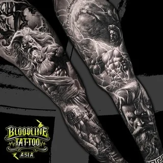 A black and grey realism full sleeve of Greek mythology with Zeus amid crackling lightning, a heroic figure, and a classical temple near the wrist, at Bloodline Tattoo Bangkok.
