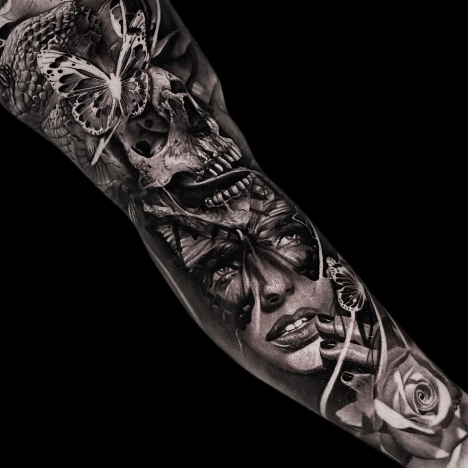 A black and grey realism sleeve montage of a human skull, butterflies across a woman's eyes, and a large rose near the wrist, at Bloodline Tattoo Bangkok.
